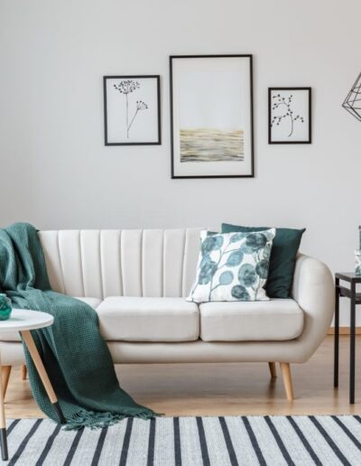 Black table next to sofa with green blanket in cozy apartment interior with gallery of posters